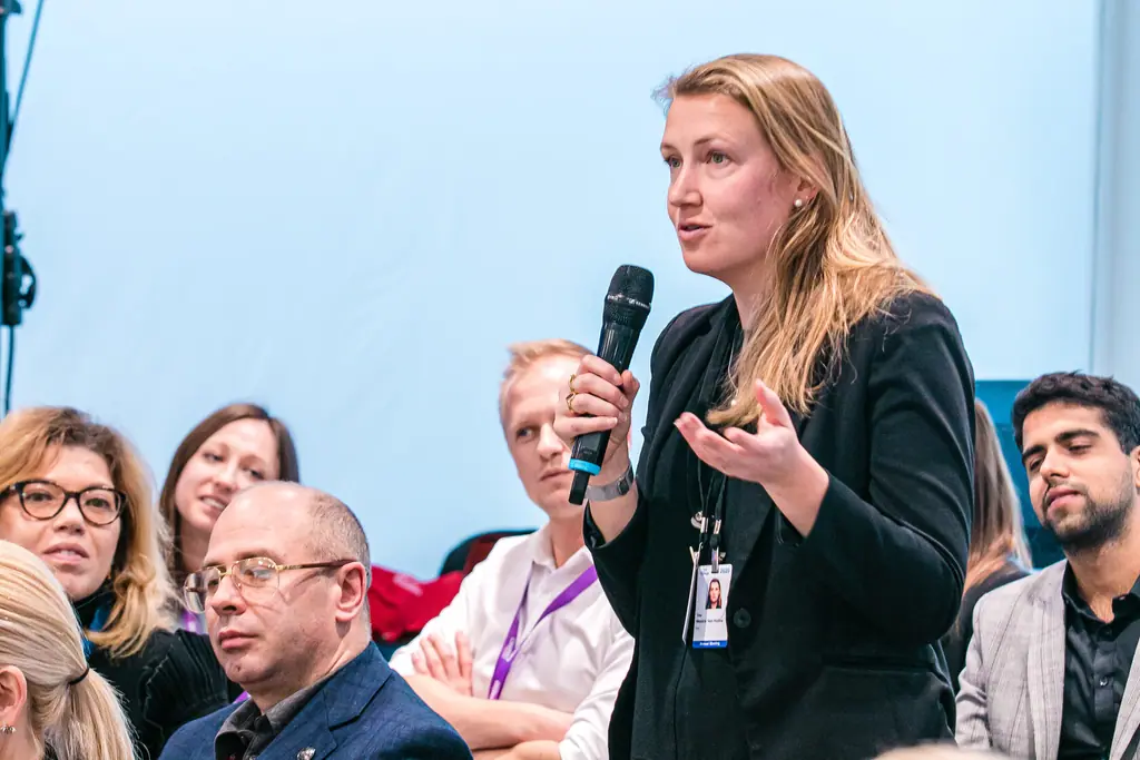 A woman stands in the audience to speak, microphone in hand