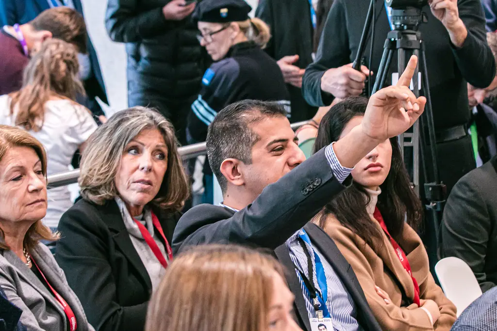 A man in the audience raises his hand to ask a question while others turn to look