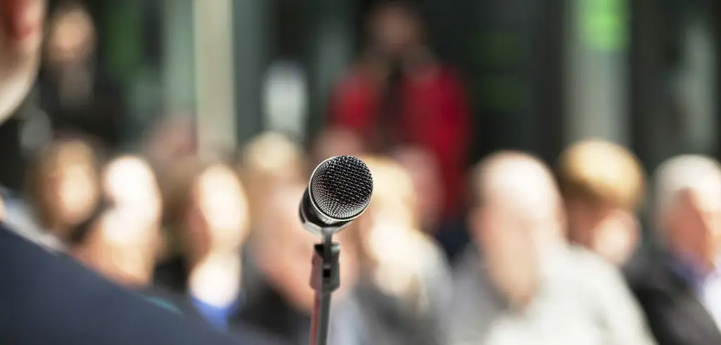 A microphone on a stand in front of an audience, out of focus